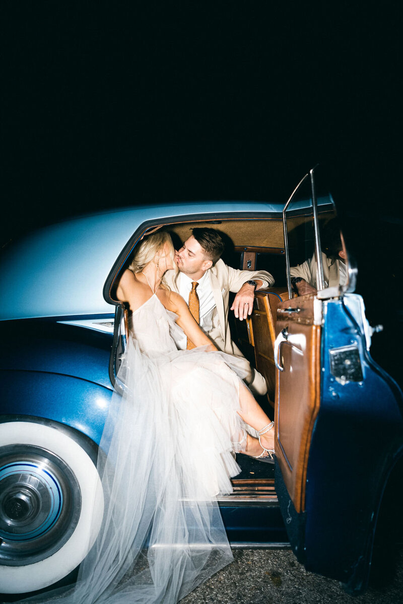 bride and groom kiss in blue getaway car at woodbine mansion