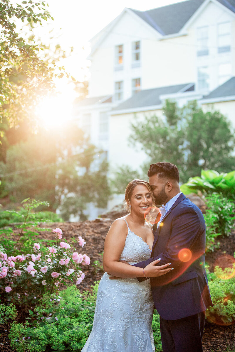 Bride and groom kiss enveloped in the golden sunset light by the waterfront, creating a romantic silhouette at Delaney House
