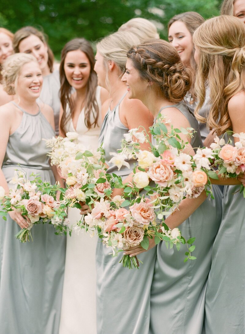 A group of bridesmaids in light green dresses holding full floral bouquets by Anthousai at the Mayo Hotel in Tulsa.