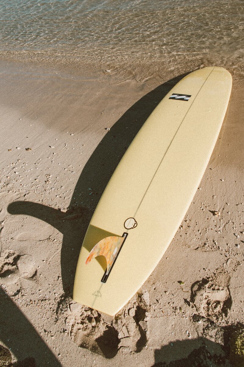 Yellow surfboard laying in the sand with Billabong sticker and surrounded by footprints