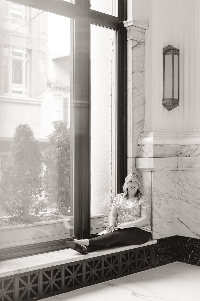 Woman sits in window sill writing in a notebook