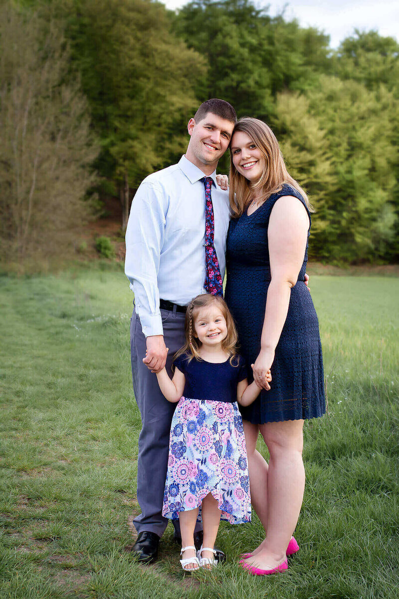 Melissa Driggers standing in a green field with her husband and daughter.