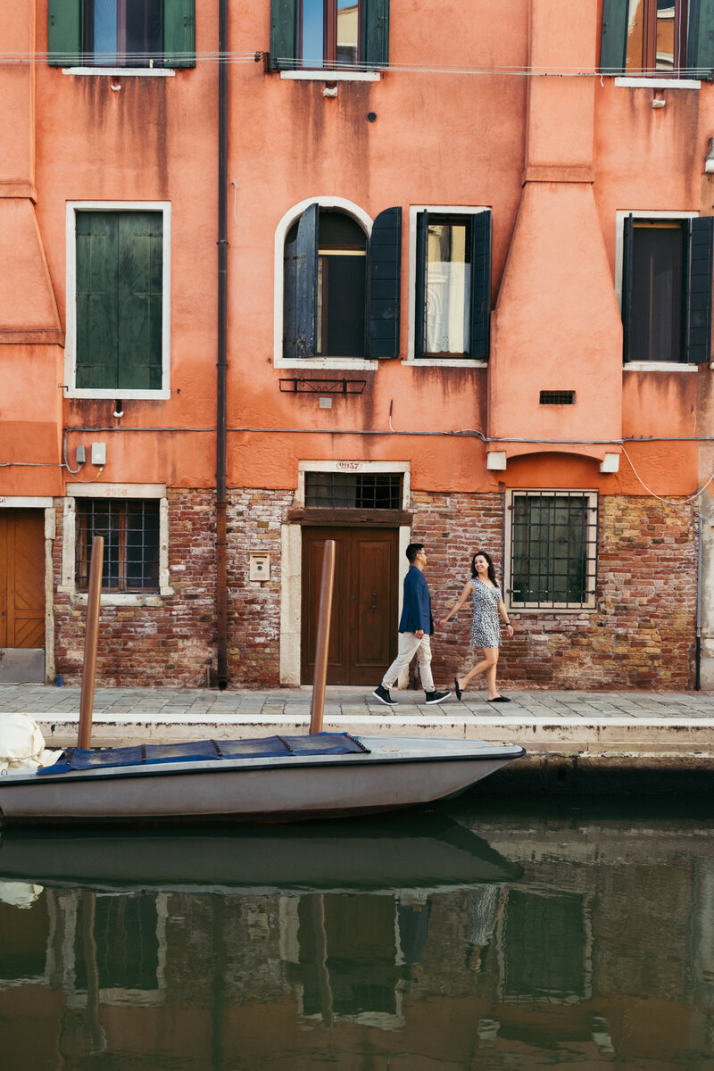 A couple walks along the picturesque Venice canal, creating a timeless scene of love and connection against the charming backdrop of the city