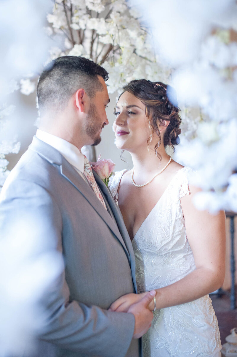 Bride in wedding gown with beading details and lace embraces a groom in pale in grey tux under white cherry blooms at eden try winery