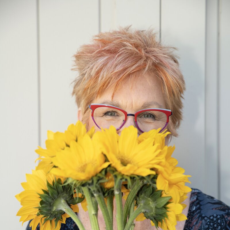 Jane Shine, blogger for Positively Jane, smiling behind a bouquet of sunflowers