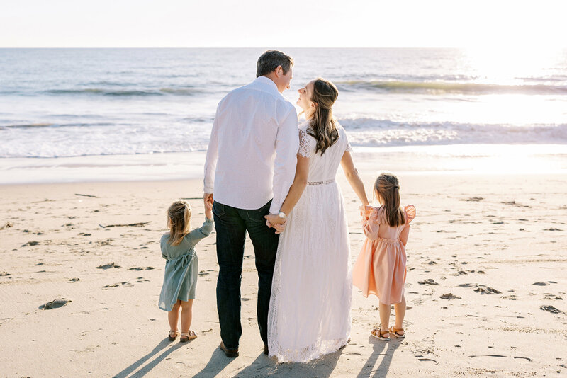 A family with two little girls hold hand on the beach during their family photos