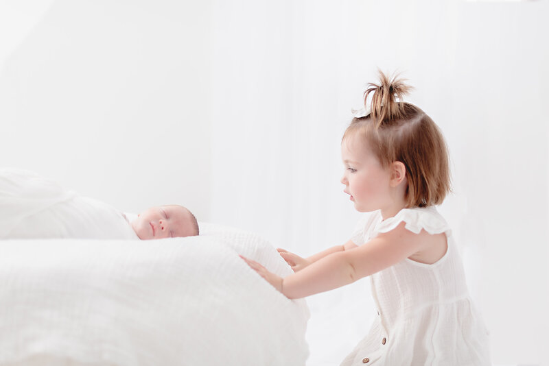 A tender moment between a big sister and her newborn sibling, taken in a St. Louis studio session.