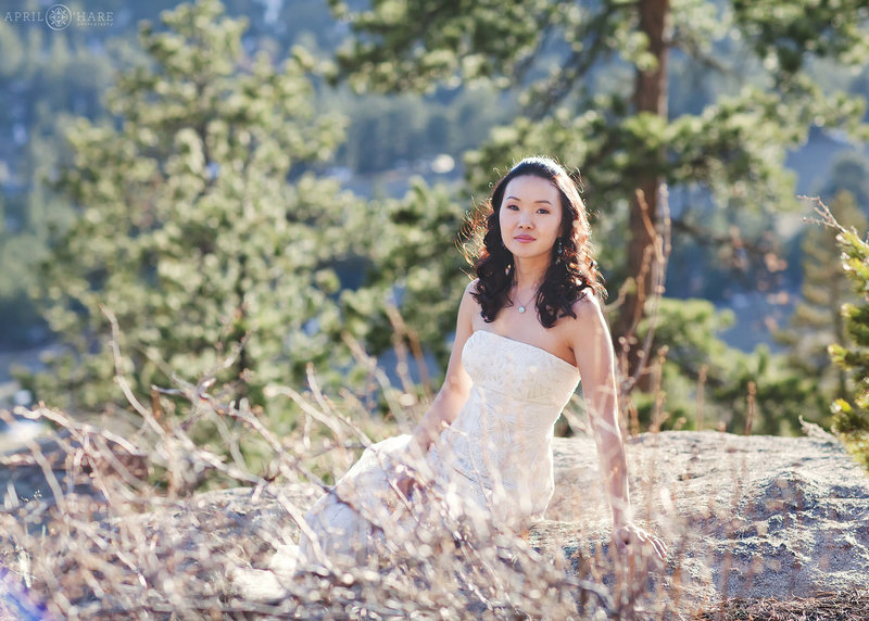Beautiful bride poses on a large rock outside of a private rental home at her Estes Park elopement in Colorado