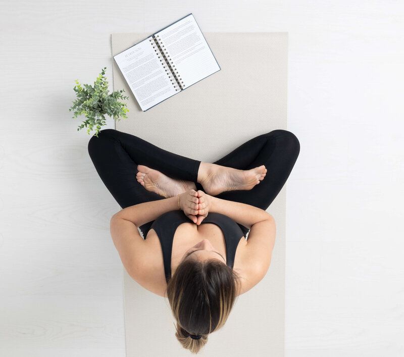 woman meditating with journal lying open in front and green plant to the side
