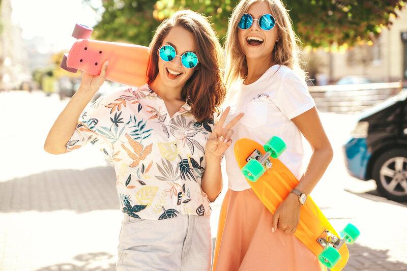 two-young-stylish-smiling-hippie-brunette-blond-women-models-summer-hipster-clothes-with-penny-skateboard-posing-surprise-face-emotions