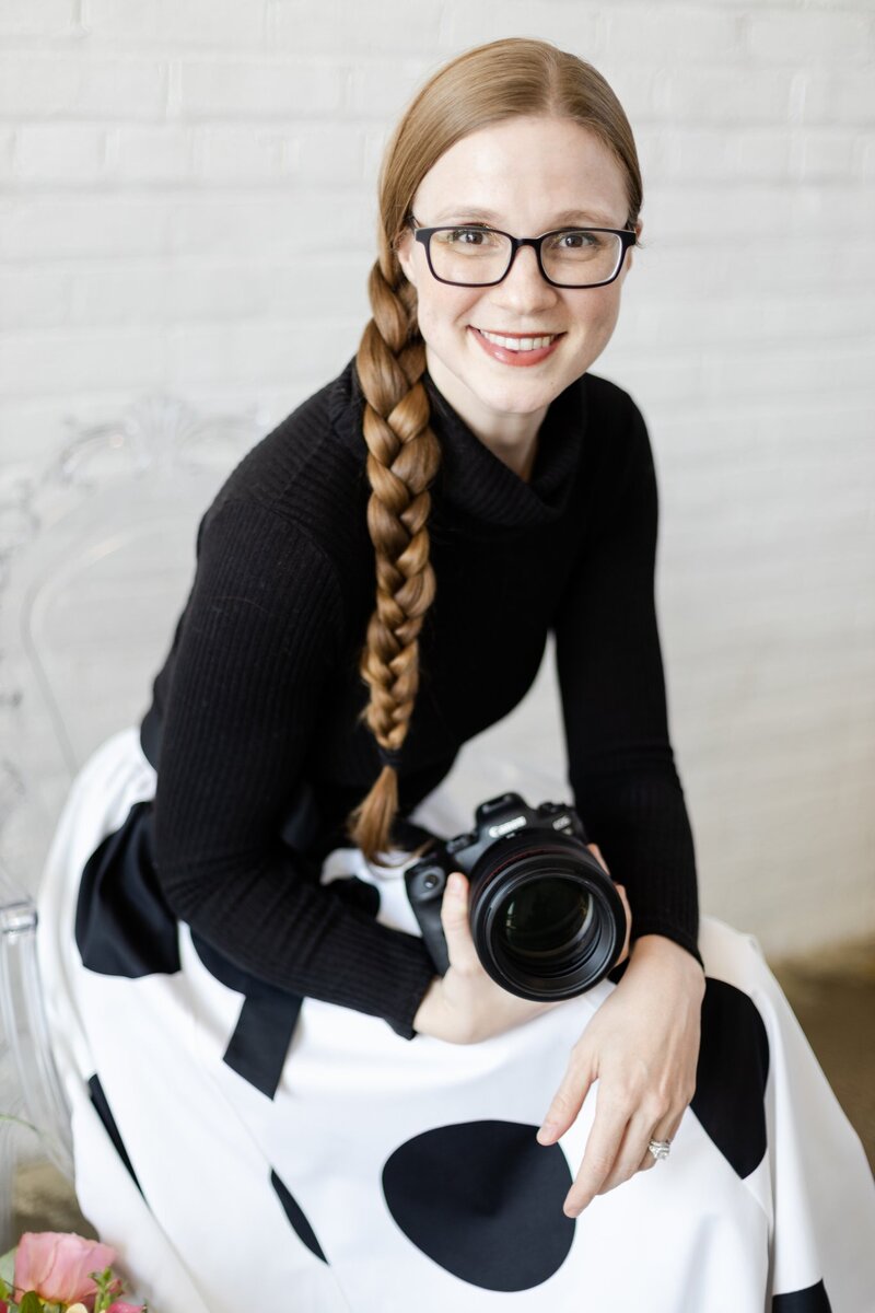headshot of Erika Cockerham- owner of Erika Rene Photography- smiling with camera in hand, wearing a polka dot dress