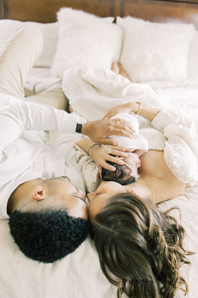 Couple snuggle on bed and cradle baby during newborn session.