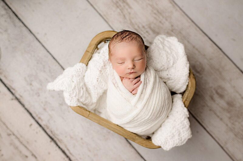 newborn baby boy is wrapped in white and posed in a basket