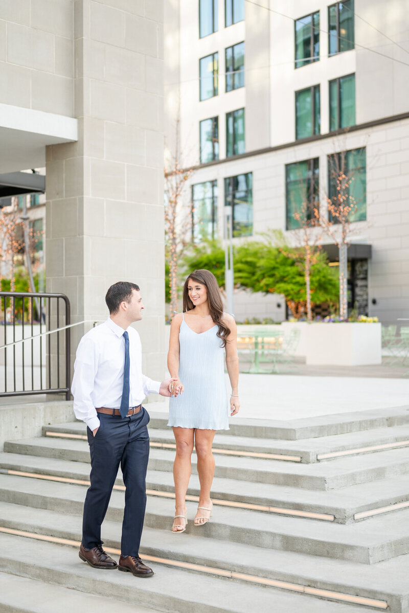 Man leads fiance down steps in downtown Greenville while they look at each other.