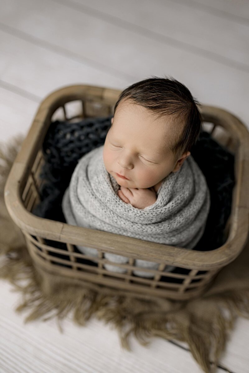 Newborn boy is wrapped in Gray and post gently in a crate with his dark hair as a feature of this image
