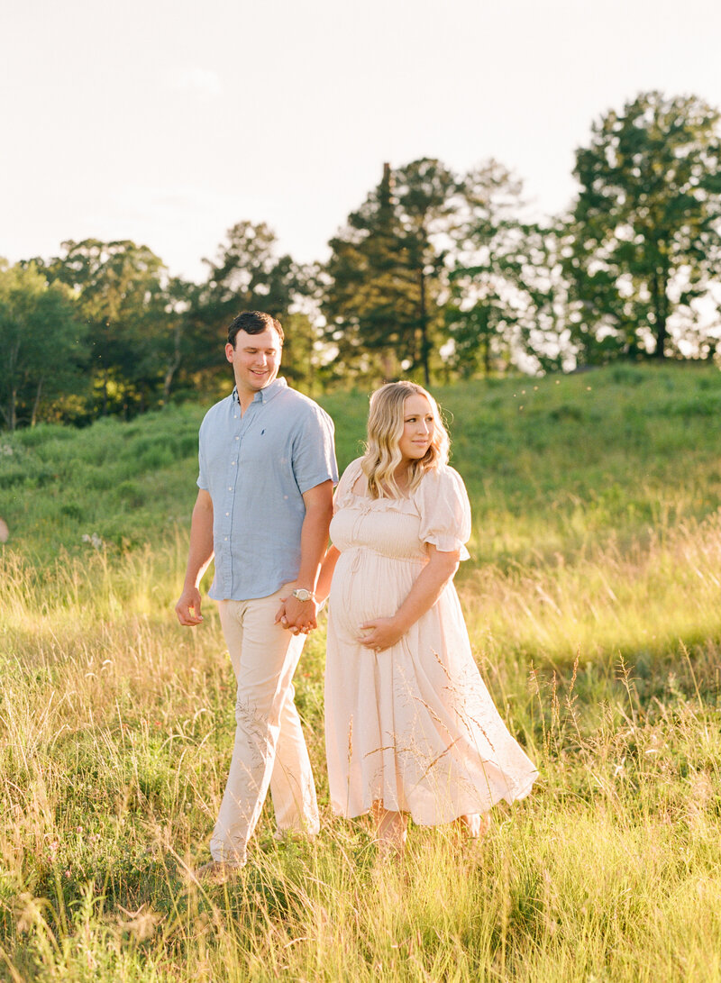 Couple walking through a field during their maternity session. Image by Raleigh family photographer A.J. Dunlap Photography.