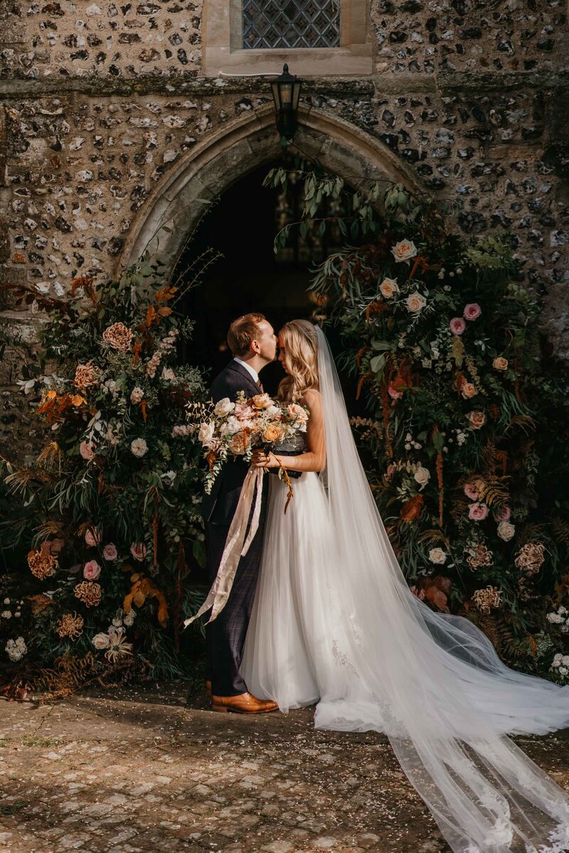 Intimate Bride & Groom outside church in front of beautiful flower arch in Hampshire