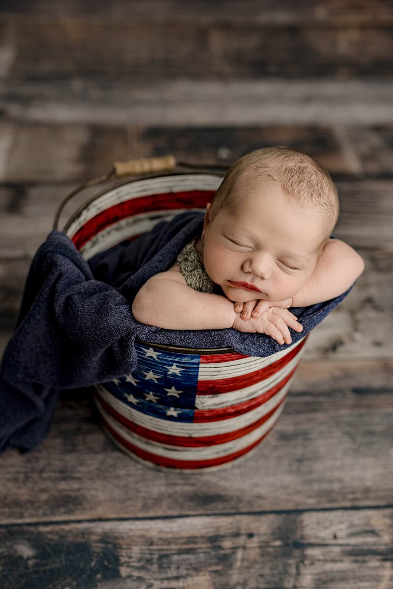 Americana themed image of newborn baby boy in a bucket with his hands underneath his cheek