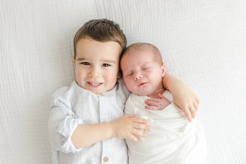 Big brother wraps his arm around his new baby brother during newborn photography session