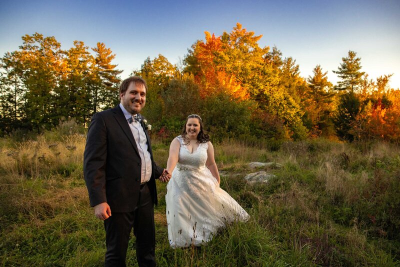 A wedding couple smiling and holding hands and they walk through a wooded area.