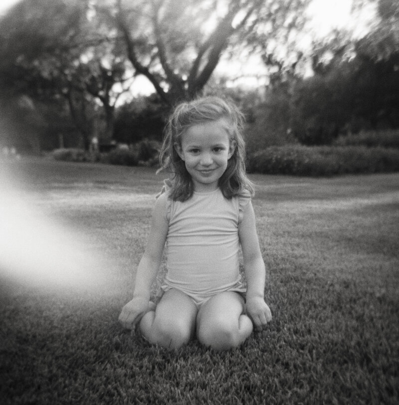 A little girl sitting on the grass in her swimsuit posing for a picture in Watercolor, Florida.