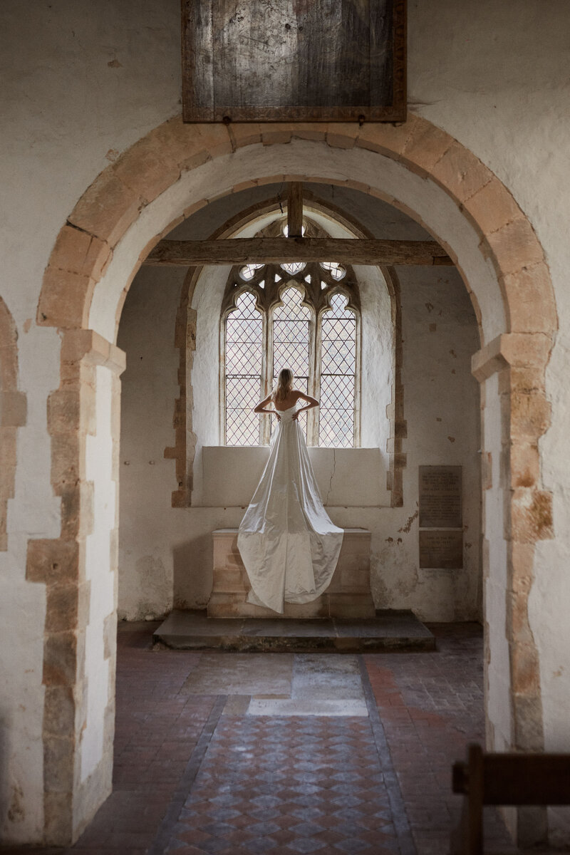 Bride wearing corset wedding dress, sleeveless style, looking our church window - photo by Benjamin Wheeler