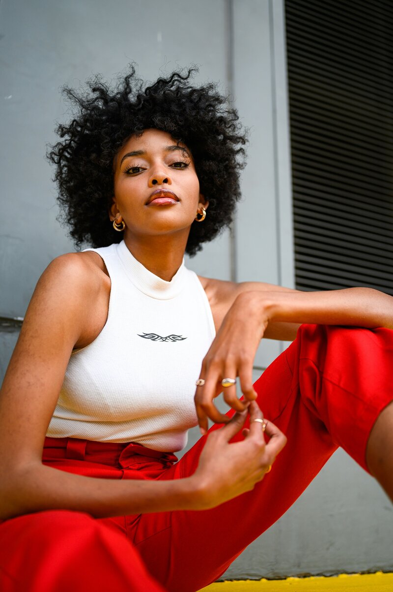 Black woman wearing white and red, posing while sitting down
