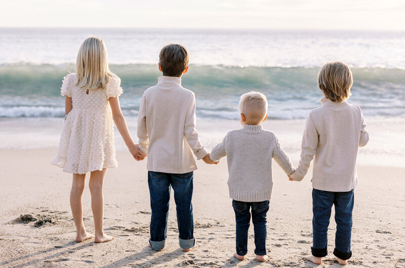 Four children holding hands while looking out at the ocean during their  portraits with Los Angeles child photographer Daniele Rose