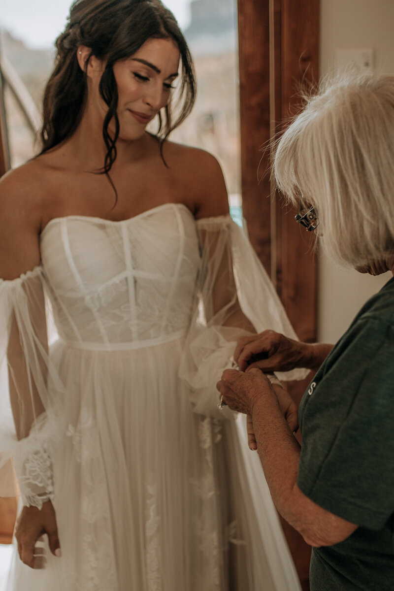 grandmother helping button the brides wedding dress with long sleeves