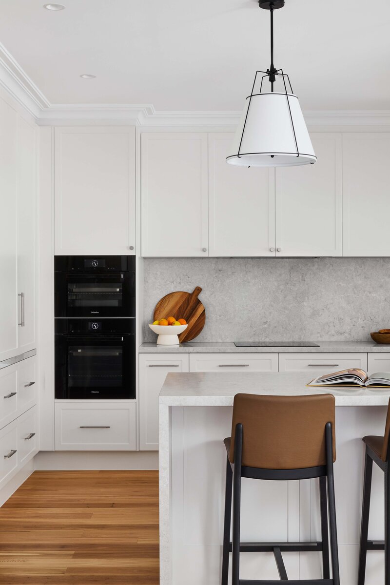 Contemporary white kitchen with marble island, timber bar stools, and integrated appliances | full service interior design for new builds