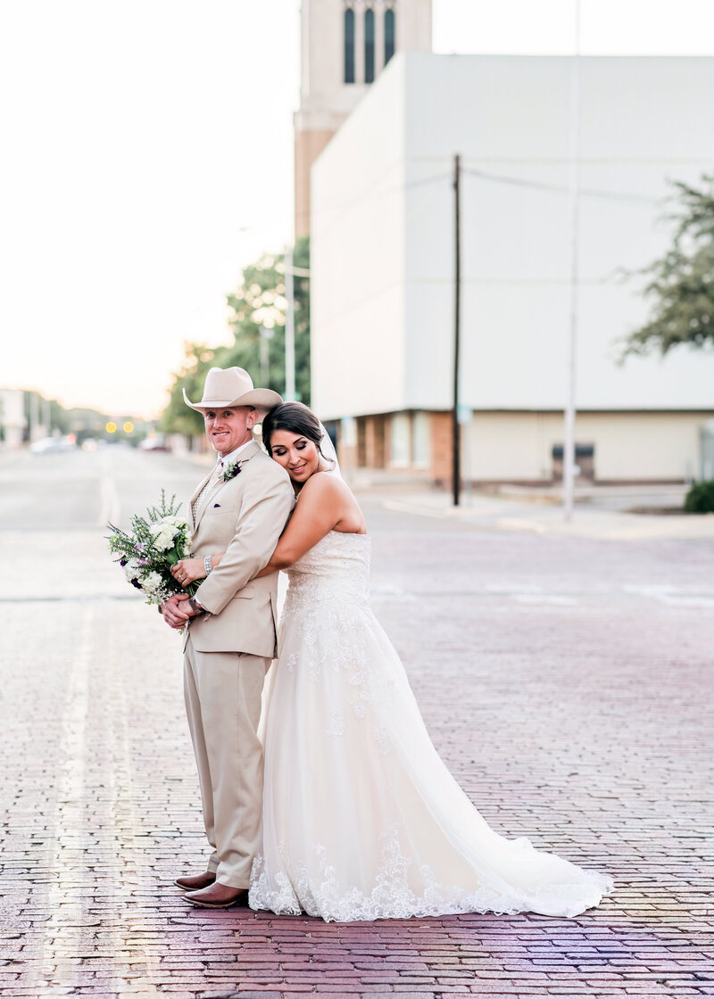Groom looking is looking at camera and bride had her eyes closed posed in downtown Lubbock TX
