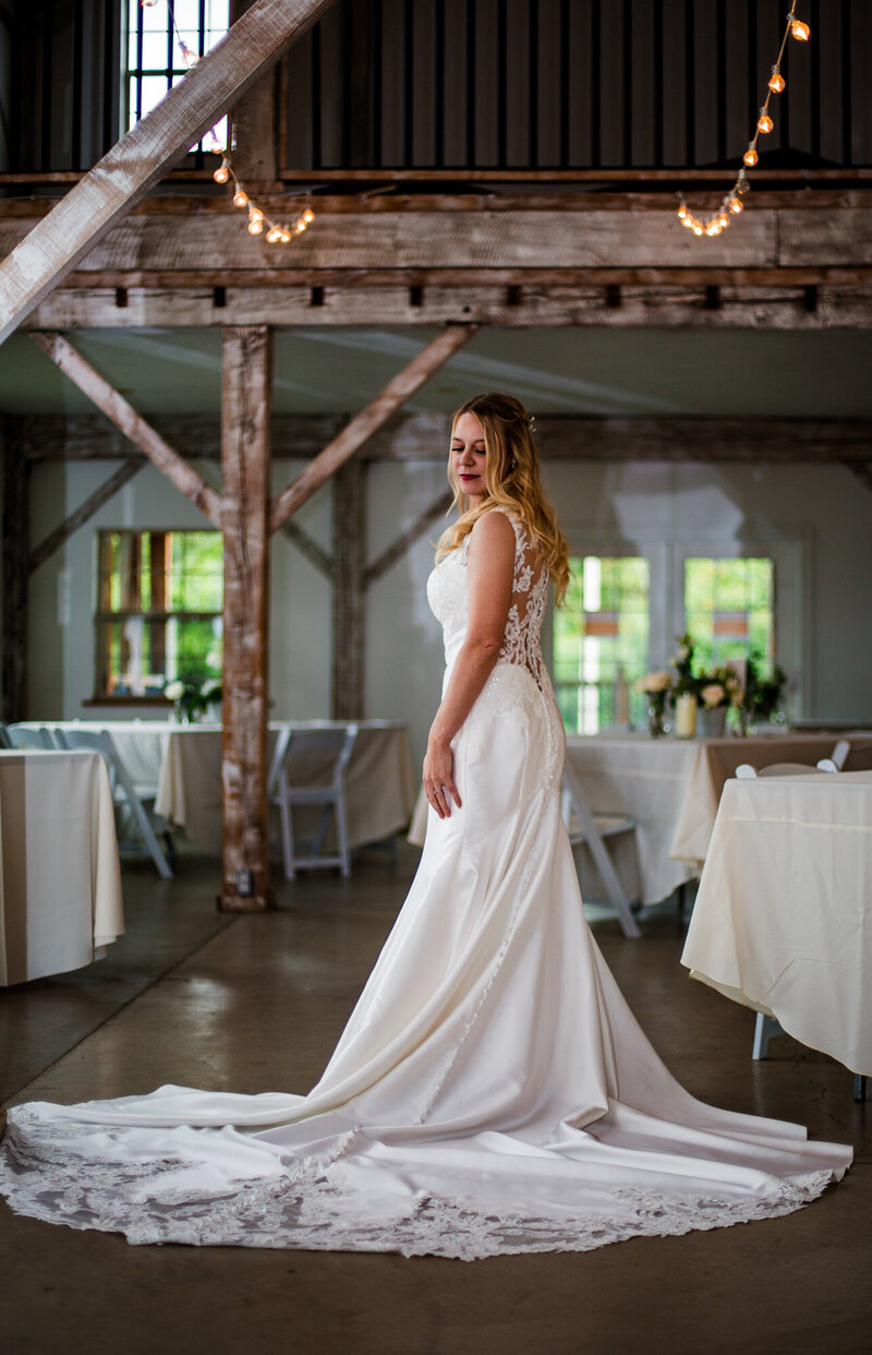 Bride stands alone in the middle of barn set up for wedding reception at Quincy Cellars
