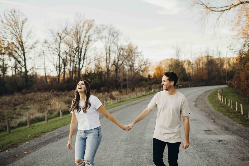engaged couple laughing and holding hands walking down a road