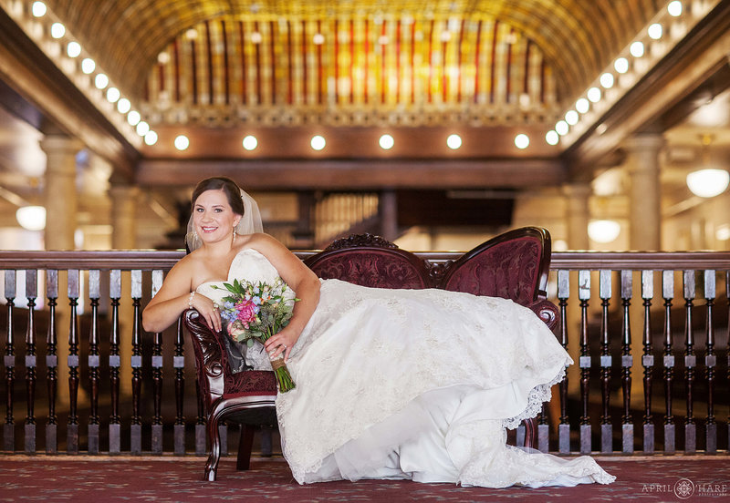 Bride lounges on a vintage settee with the stained glass skylights in the backdrop at Hotel Boulderado on her wedding day