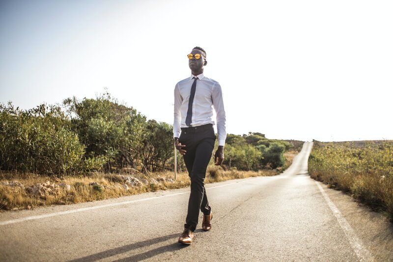 A professional, black man walking down the road in his work clothers.