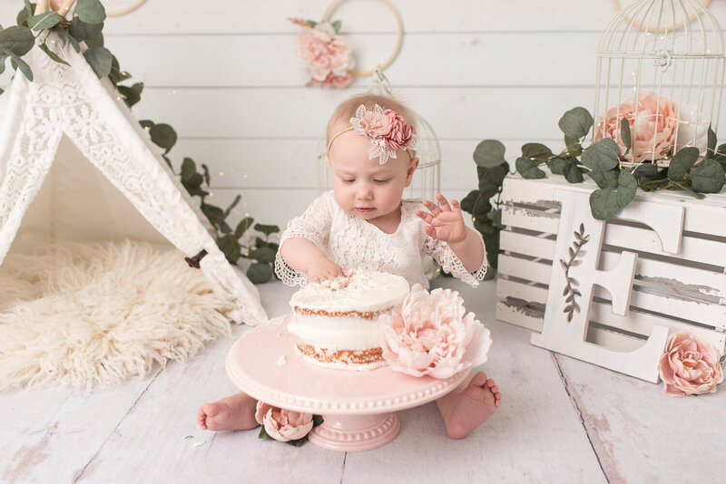 Little girl in pink smiling at camera with cake for first birthday photo session