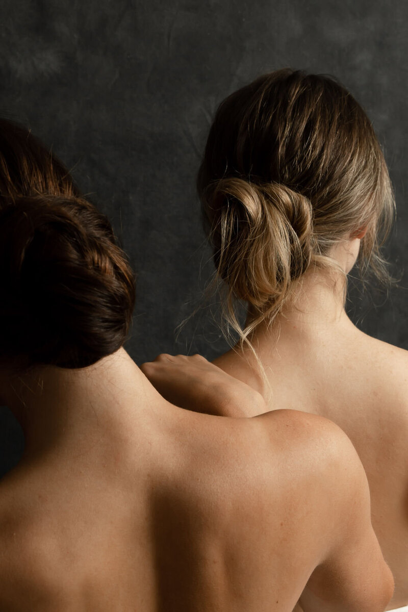 Backside of two bridal hairstyles, one brunette updo and one blonde updo
