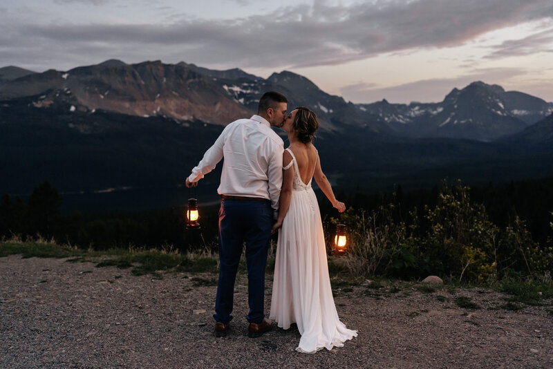 Montana Wedding Photographer. A wedding couple holds lanterns and kisses in front of a mountain view during blue hour.