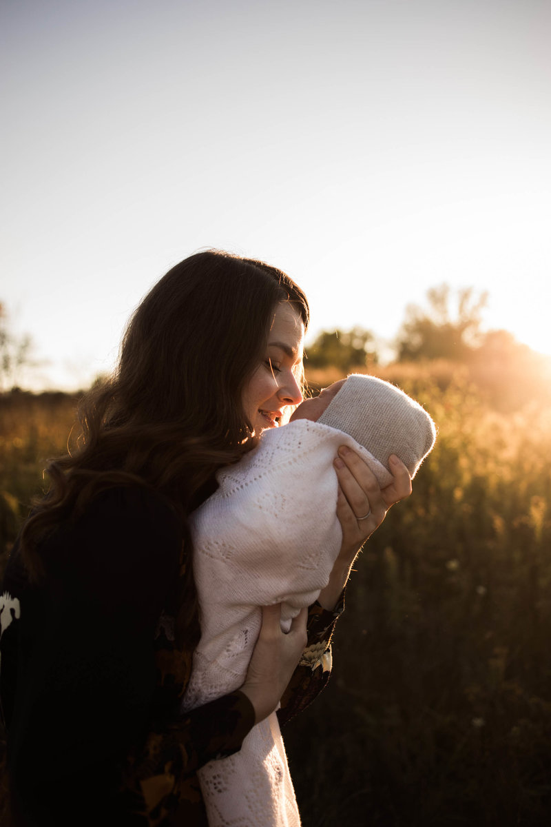 Mother holding her newborn baby outdoors at sunset, photo taken by Elle Baker Photography