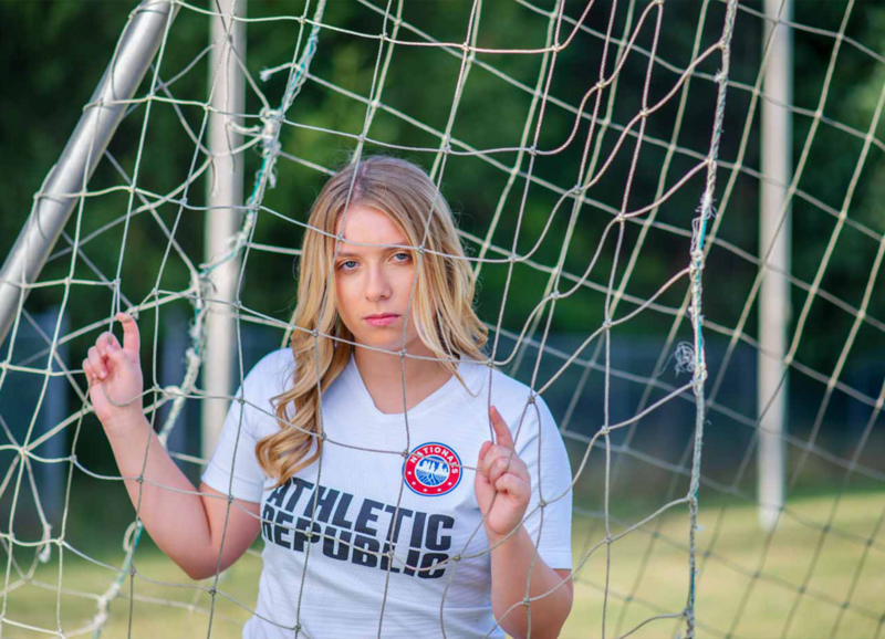 close up of high school senior girl posed behind soccer net holding the net