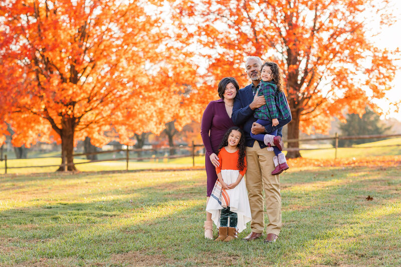 A family of four smiling at the camera during their fall photos in Burke, Virginia.