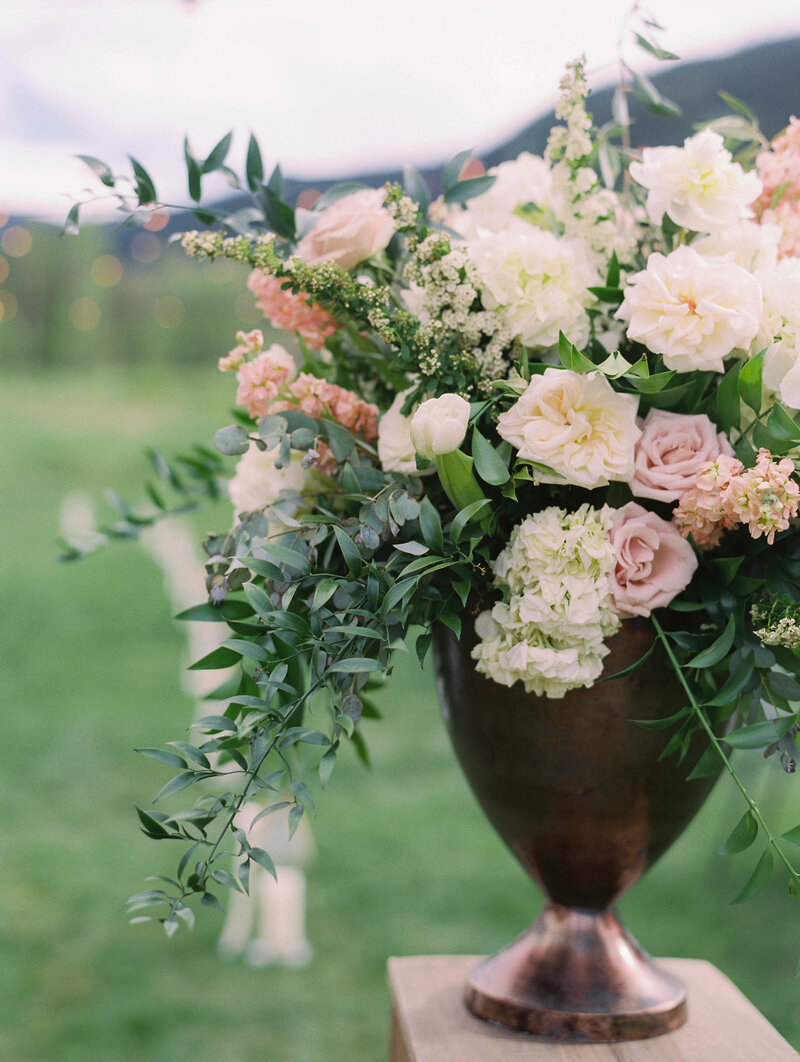 Testimonial photo, a large bouquet of pink roses, white flowers, and long green stems in a bronze vase