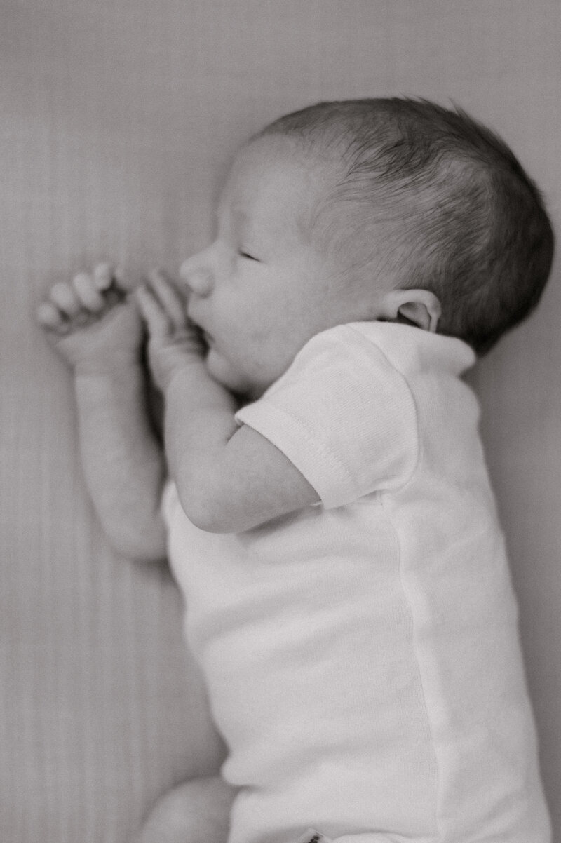 A newborn boy sleeping on his side with his hands close to his face