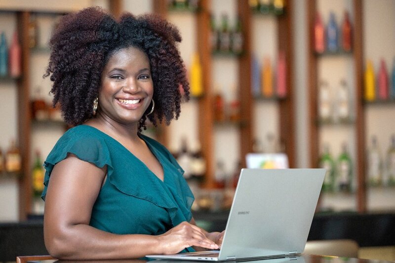 A smiling  destination wedding planner using a laptop at a bar.