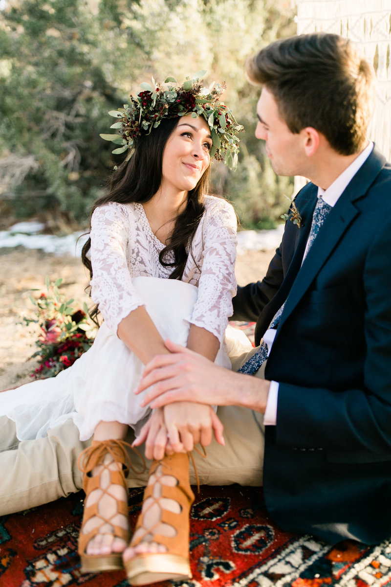 Bride looks up at her groom as they sit on a brightly patterned  boho rug.