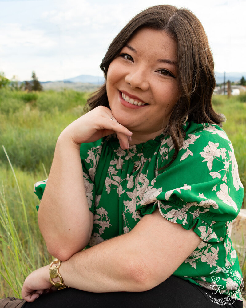 Photo of Ashlyn in a green floral shirt, sitting with her chin resting on her right hand