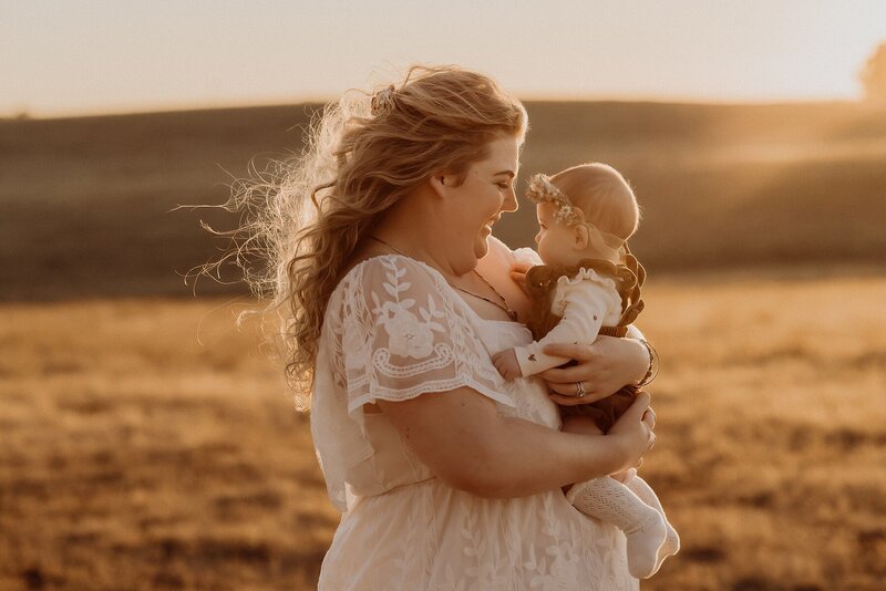 A woman holding her baby in a field at sunset.