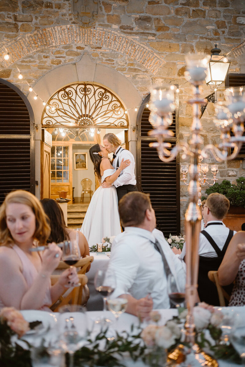 A kiss during the wedding dinner under some bulbs lights in Borgo Castelvecchi, in Tuscany