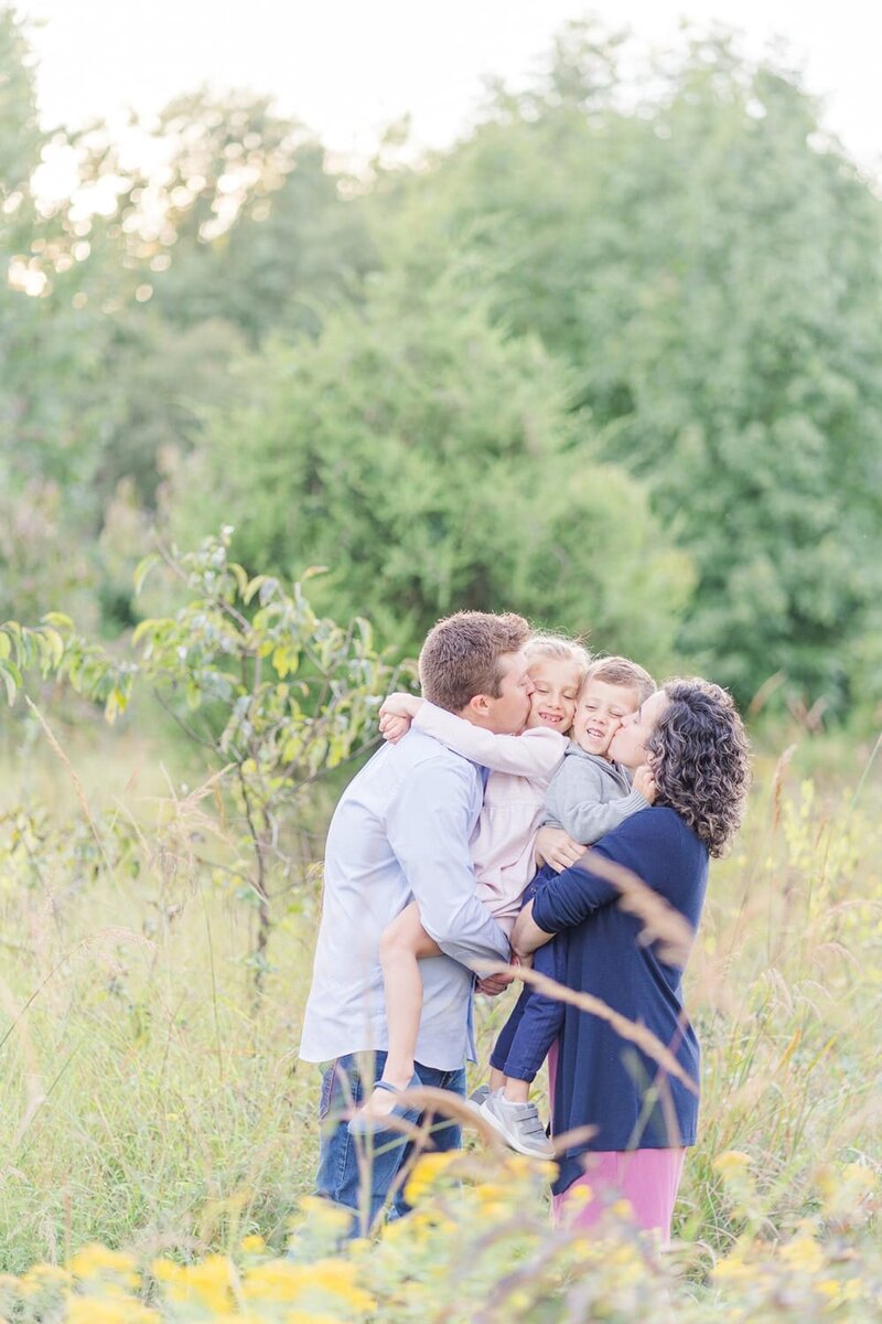 mom and dad kissing kids during their family photos in Sterling, VA by a family photographer in Northern Virginia