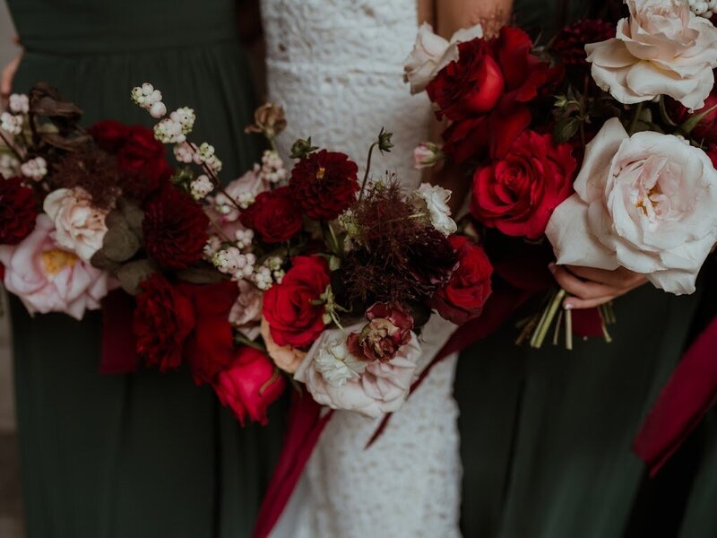 A bride and two bridesmaids carry bouquets of burgundy, cherry red and blush against their hunter green dresses at Lago venue in Ottawa Ontario